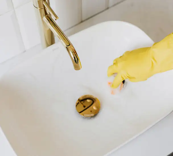 Gloved hand cleaning a sink with eco-friendly products